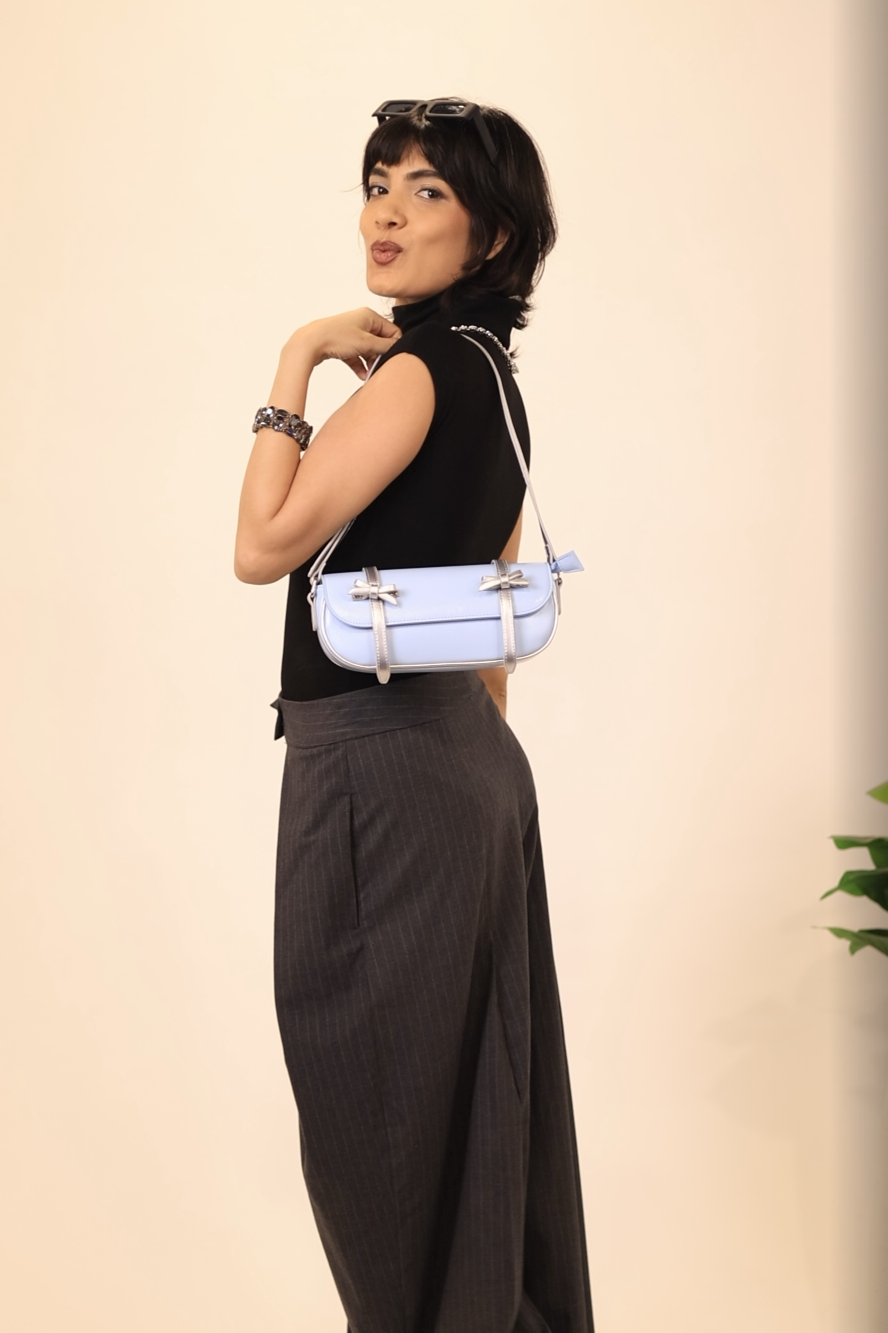 Woman wearing a black sleeveless top and wide-leg pants, holding a reflective handbag against a beige background.
