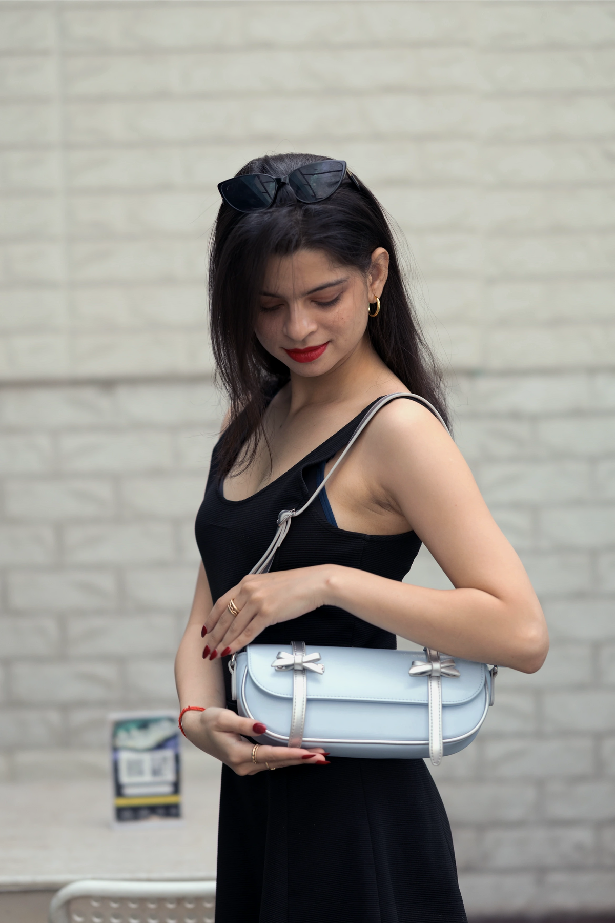 Woman holding a light blue handbag against a gray brick wall.